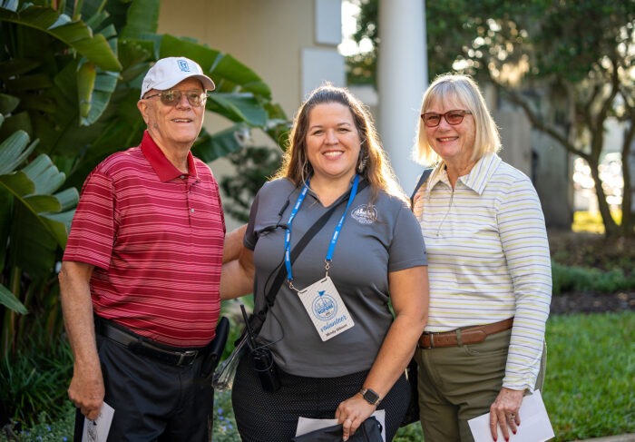 Two attendees and a female employee smiling and posing together at the Money Pages Charity Golf Classic event.