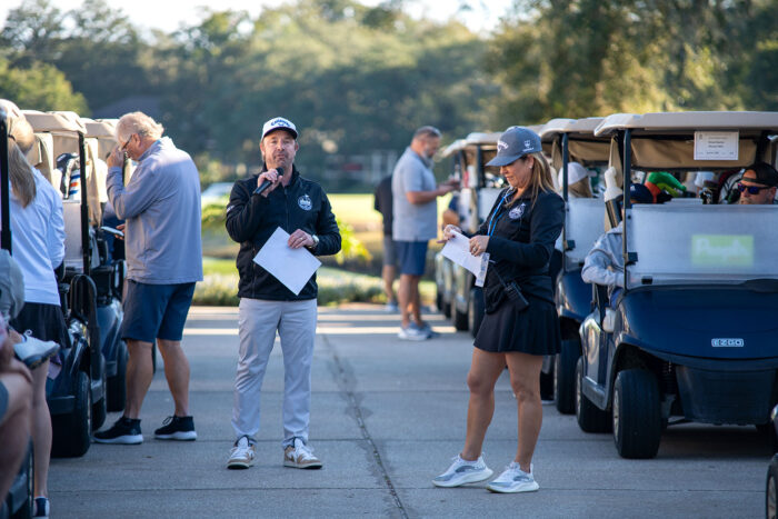 Event organizer addressing golfers with a microphone at the start of the Money Pages Charity Golf Classic.