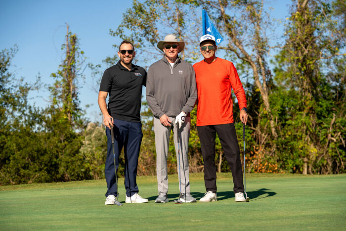 Three golfers posing together on the green with clubs during the Money Pages Charity Golf Classic.