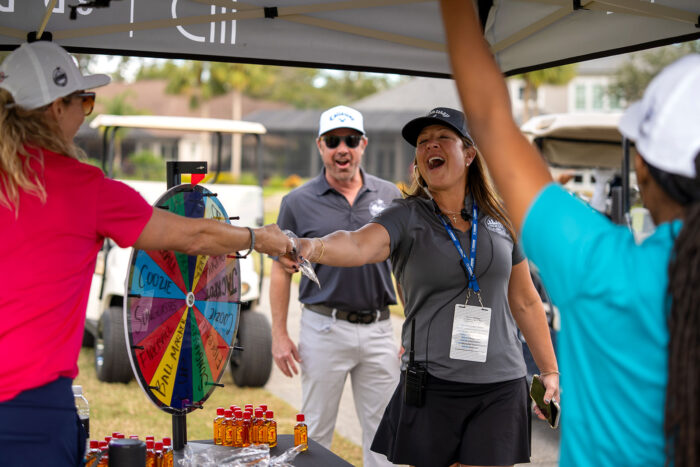 Volunteers spinning a prize wheel at the Money Pages Charity Golf Classic booth, sharing laughs and giveaways.