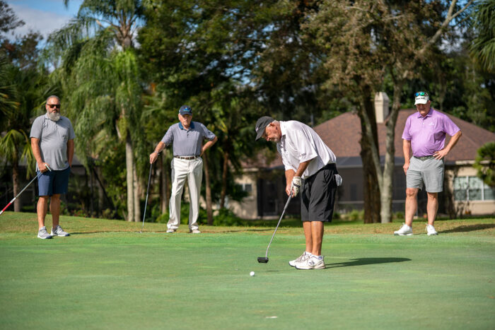 Group of golfers watching a participant putt on the green during the Money Pages Charity Golf Classic.