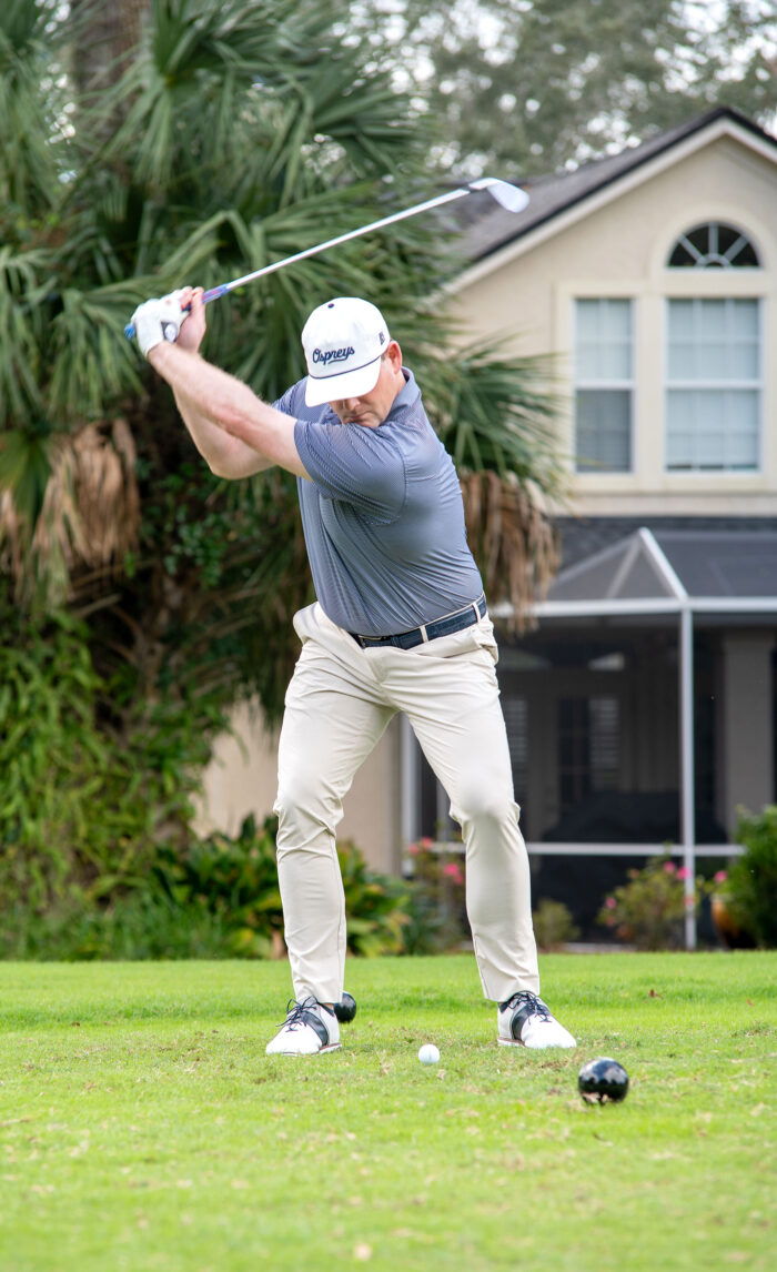 Golfer in mid-swing on a lush fairway with a residential backdrop at the Money Pages Charity Golf Classic.